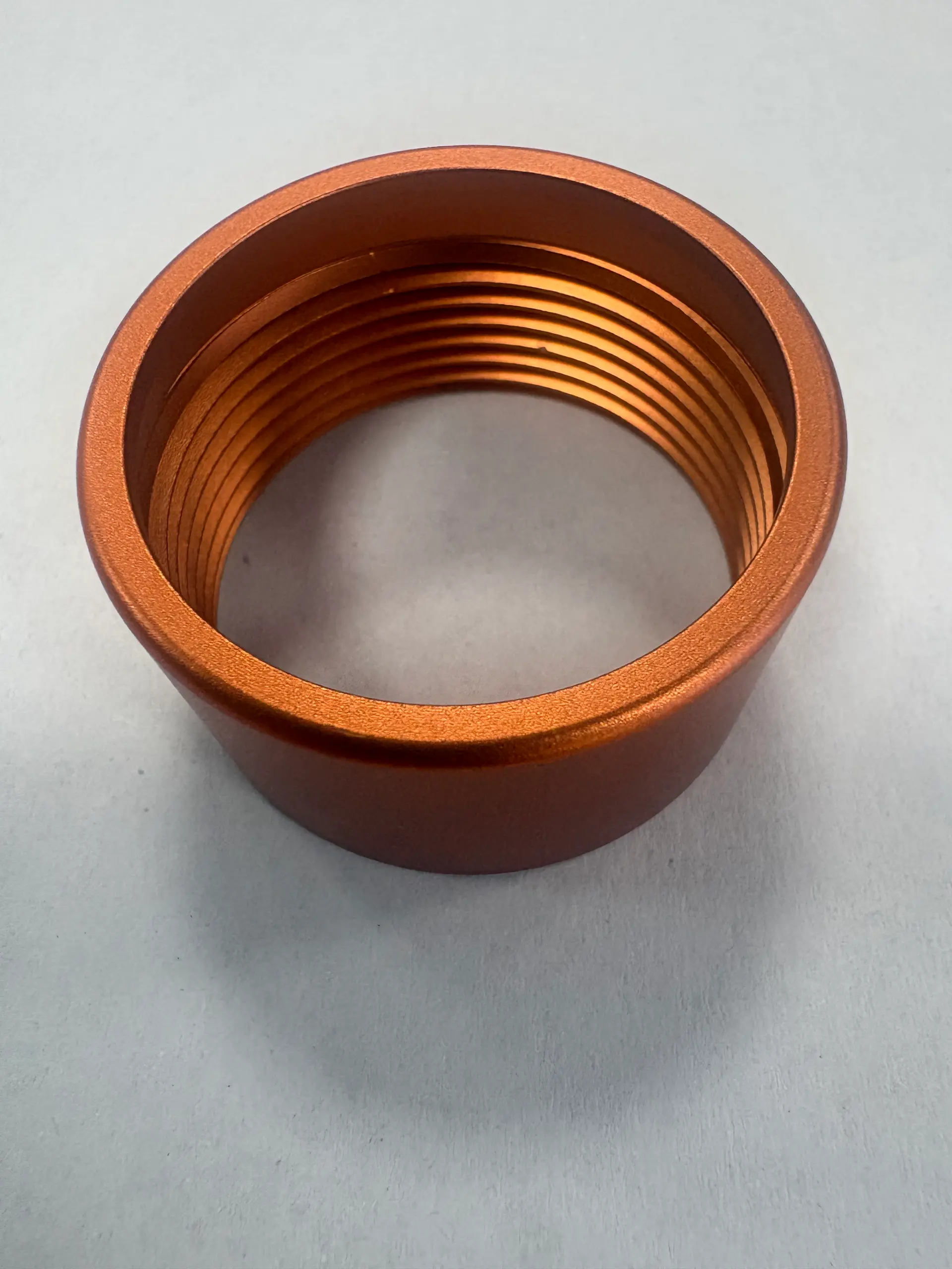Orange anodized aluminum threaded ring with visible internal machined grooves